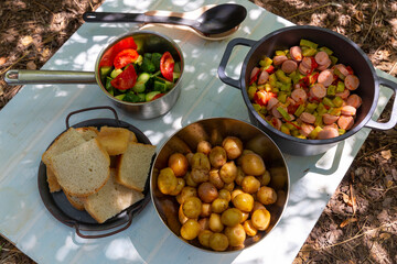 Tourist’s lunch at the campsite. Sausages with zucchini and tomatoes, jacket potatoes and tomato and cucumbers salad.
