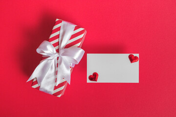 Gift box with blank card and hearts on a red background. Valentine's day concept.