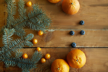 Fir branches on a light wooden background decorated with tangerines and blueberries. Top view. Christmas concept. High quality photo