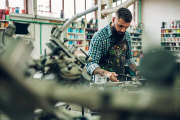 Male worker pressing ink on frame while using the printing machine in a workshop