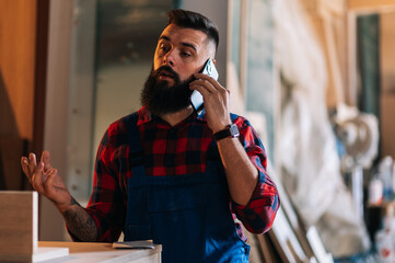 Young male carpenter working in workshop and using smartphone