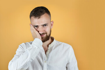 A young man on an orange background complains of toothache, from the tooth and head began to ache, the man needs to go to the dentist more often. The man is holding his cheek