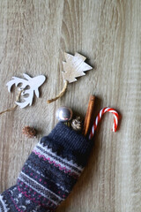 Wool stocking filled with small Christmas ornaments, cinnamon stick and candy cane. Wooden background, flat lay.