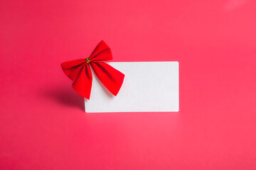 Blank card with a red bow on a pink background. The concept of postcards, business cards. With copy space