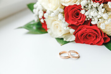 Gold wedding rings and flowers bouquet in white red colors lying on white background. Declaration of love, spring. Wedding card, Valentine's Day greeting. Wedding rings. Wedding day details