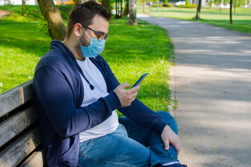 Young man with face mask using mobile phone in the park