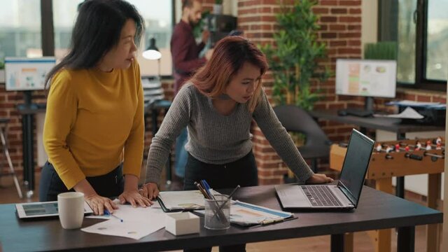 Business partners looking at marketing analysis on laptop, doing research to plan new project application for financial growth. Asian women using sales statistics to work on management