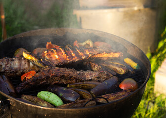 Pork ribs and various vegetables cooking on barbecue grill with smoke and flames for summer outdoor party.