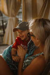 Mom at the pool laying in lawn chair tickling son and  laughing with sun shining through 