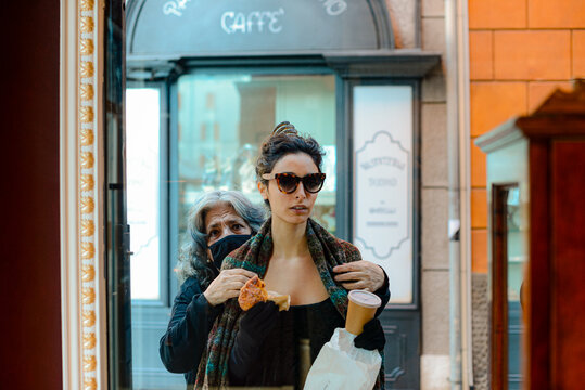 old woman helping young woman wearing a tube dress and sunglasses putting a scarf in the street