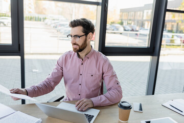 Businessman working with documents near devices and coffee in office.