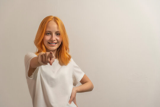 teen girl with red hair in a white t-shirt on a light background point finger forward