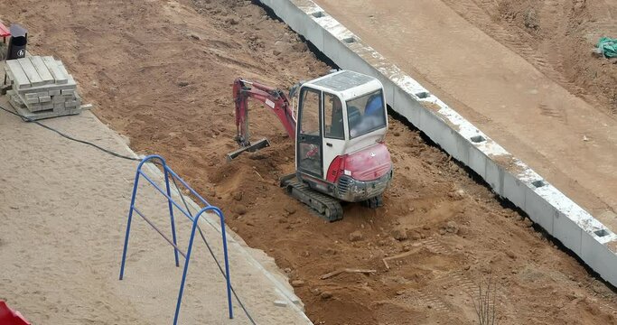 A small excavator works on the construction site of a building. The excavator loads the sand.