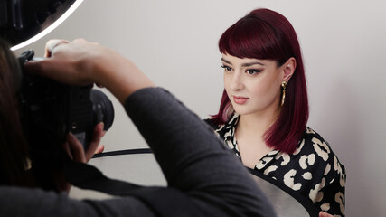 Professional photographer and a beautiful red head model on fashion shoot in photo studio with ring light equipment. 