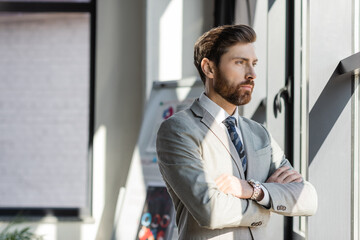 Fototapeta premium Businessman in suit crossing arms near window in office.