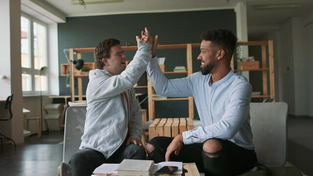 Young man with Down syndrome and his tutor studying and celebrating success indoors at school.