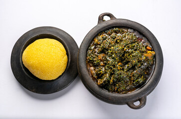 Efik Afang soup Nigerian served in a clay bowl with garri on a white background