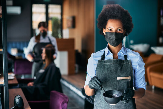 Black hairdresser wears face mask while working at hair salon during coronavirus pandemic.