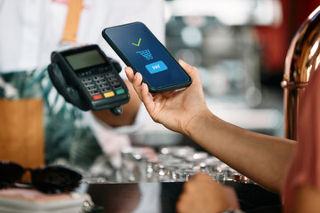 Close-up of woman uses smart phone while making contactless payment at bar.