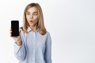 Little girl, blond teen child showing empty phone screen, mobile phone interface, video game on application, standing happy against white background