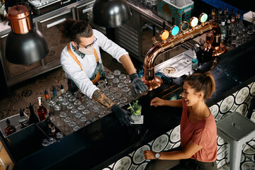 Above view of barman serving cocktail to female customer at bar counter while and wearing face mask...