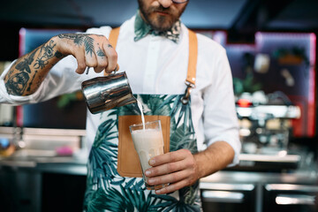 Close-up of barista adding milk while making coffee.