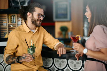 Young happy couple talks while drinking cocktails at bar counter in a bar.