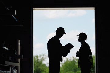 Silhouette of two workers analyzing paperwork in warehouse.