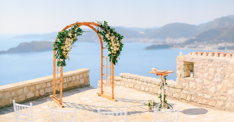 Wooden wedding arch decorated with flowers stands on the observation deck above the sea
