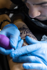 closeup vertical portrait of a tattoo artist wearing blue gloves performing a tattoo