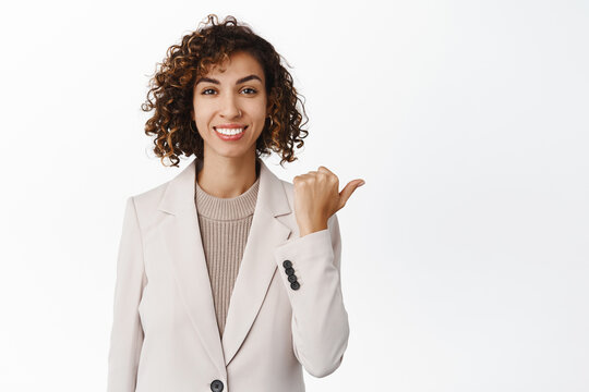 Successful real estate agent, female entrepreneur pointing right, showing company logo, brand name, standing in suit over white background