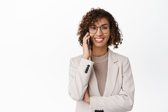 Image of stylish corporate woman talking on smartphone, making a phone call, wearing business suit and glasses, standing against white background