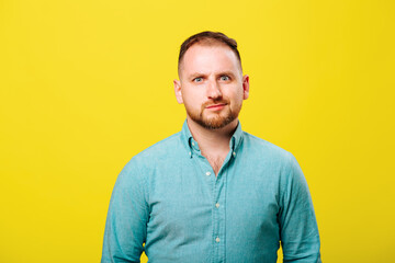 portrait of a bearded young man looking at the camera suspiciously in the studio on a yellow...