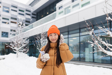 Young beautiful Asian woman listens to music from headphones while walking on a winter snowy day,...
