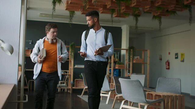 Young man with Down syndrome and his tutor walking together indoors at school.