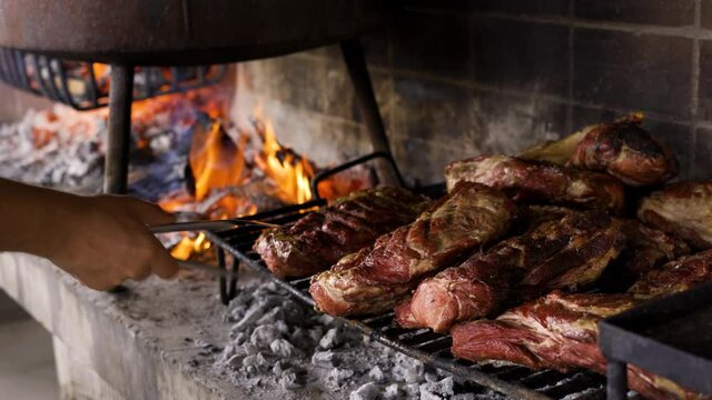Chef controlando el punto de cocci&oacute;n de la carne sobre una parrilla al fuego. T&iacute;pico asado Argentino.