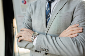 Cropped view of businessman standing with crossed arms in office.