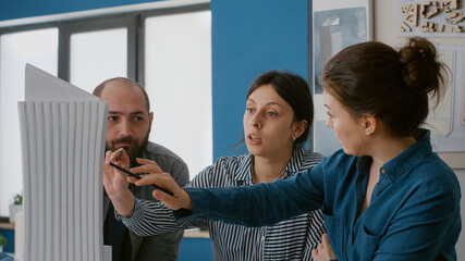 Close up of coworkers analyzing building model and maquette to plan construction structure. Team of people working together on urban blueprints to design real estate property.