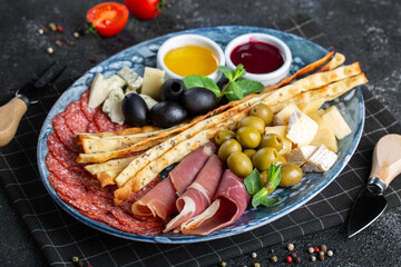 Assorted Italian appetizers with grissini on a plate. Sausage, ham, olives, cheese.