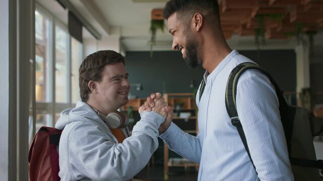 Young man with Down syndrome and his tutor greeting and looking at camera indoors at school.