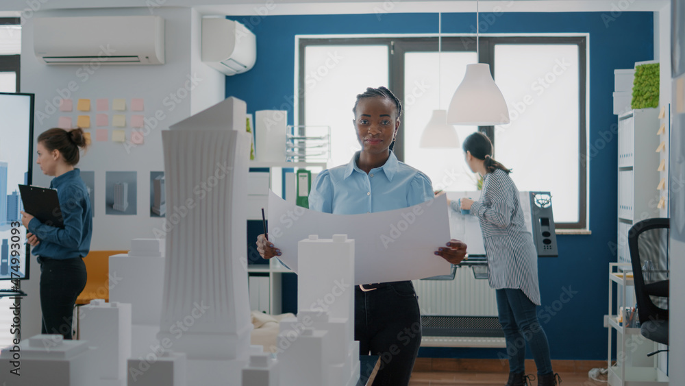 Poster portrait of woman architect analyzing blueprints plans on paper to design building model and maquett