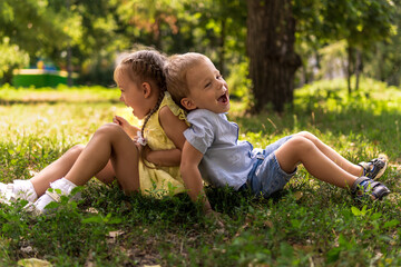 Fototapeta premium Two happy smiling cheerful toddler preschool twins siblings children brother sister boy girl sitting together on grass lawn in park in sunny hot summer weather. childhood, friendship, family concept