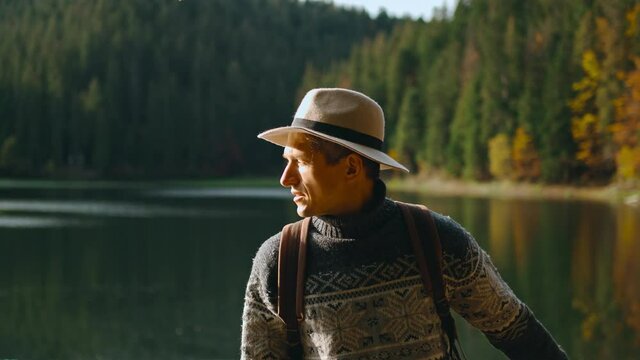 Traveler hipster man in hat standing on pier and admiring mountain lake among forest. Traveling to the wild nature beauty location.
