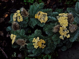 Decorative autumnal grave arrangement made up of green fir branches, yellow dried flowers of the yarrow and dry spots rustic brown prickly cards. Handcrafted and compiled.