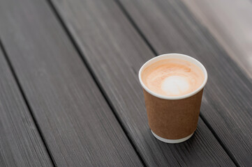 Takeaway paper cup with cappuccino or latte close up and copy space. Wooden dark textured rustic table..