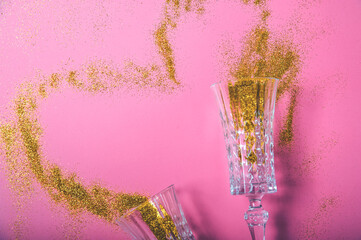 Two champagne glasses and gold glitter on pink background. Concept of holiday for couple.