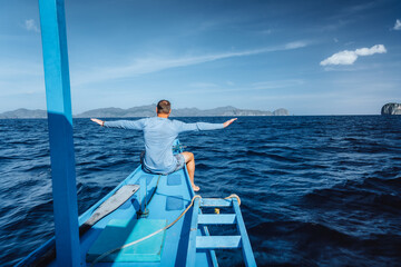 Back view of the man on boat with spreading hands arriving to exotic tropical island lit by sun light. Travelling tour in Asia: El Nido, Palawan, Philippines