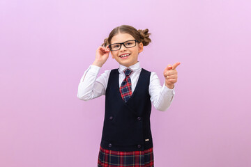 A joyful schoolgirl with glasses points her finger at the advertisement. A student in a school uniform on a purple isolated background. Space for copying.