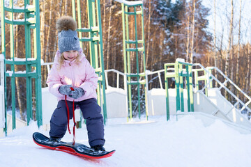 little cute girl learning to ride a children's snowboard, winter sports for the child, safety of...