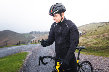 Young caucasian cyclist man using a smartphone on his bike in the top of a mountain.